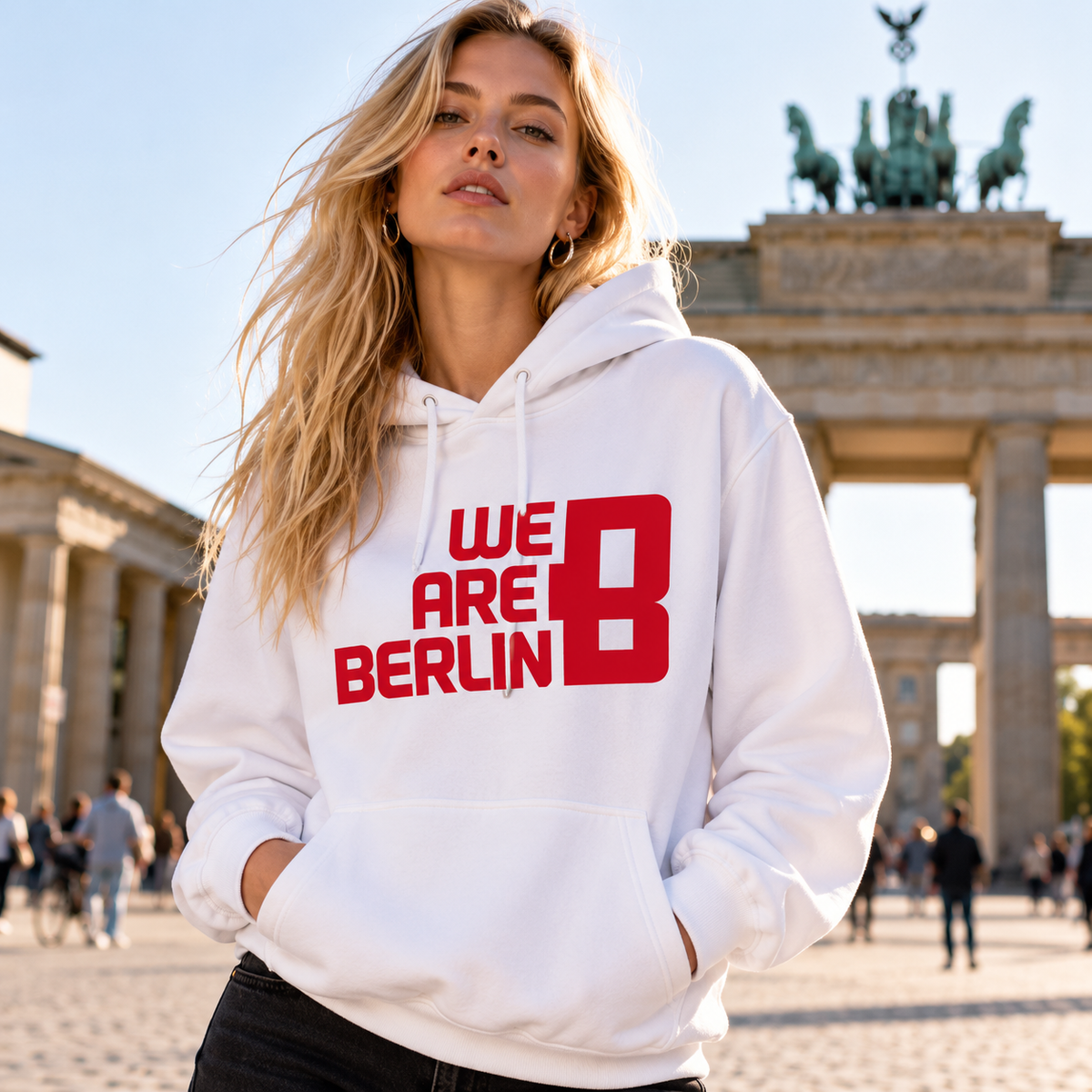 Model mit weißem WE ARE BERLIN Hoodie und rotem Brustlogo vor dem Brandenburger Tor